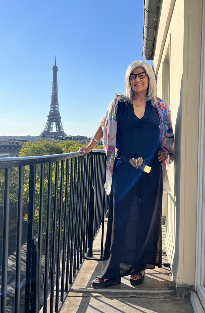 woman standing on balcony with the eiffel tower in the background. Showing her style